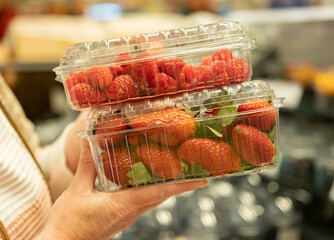 Raspberries and strawberries in containers in person's hand on blurred background of supermarket shelves close-up.