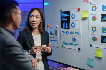 Business professionals engage in a data analysis discussion in a modern office setting. Charts and...
