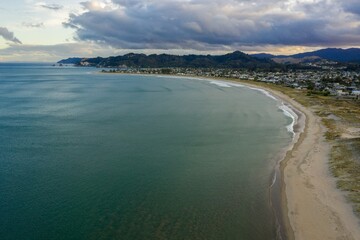 Coastal Whangamata town nestled beside a tranquil beach. Houses line the shore, reflecting the calm ocean. Aerial view.  Coromandel Peninsula, New Zealand