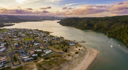 Aerial view of Whangamata town with boats in a river estuary. Houses line the shore, and a small...