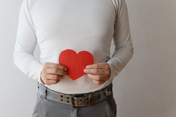 Man holding a red heart symbol in front of a neutral background while expressing love