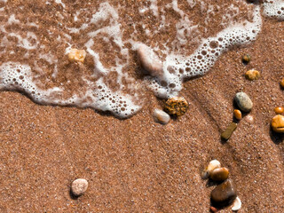Shoreline close up with waves and pebbles on sandy beach
