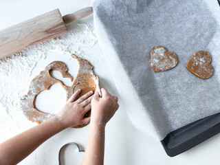 Child baking gingerbread cookies with heart shapes on floured surface