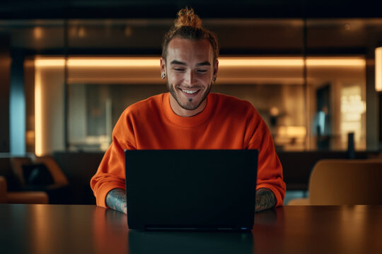 Young man enjoying leisure time while working on laptop in modern interior at night