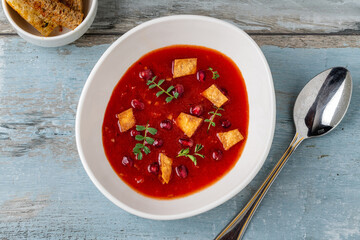 Red soup with pomegranate seeds, croutons, and fresh herbs in a bowl