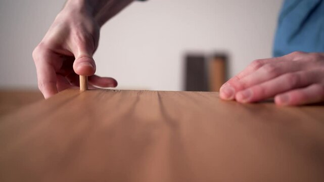 man assembling a DIY furniture, putting wooden dowel in shelf part