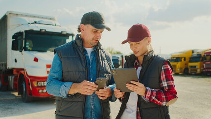 Caucasian man and woman standing at truck pit stop. Discussing something while looking at...