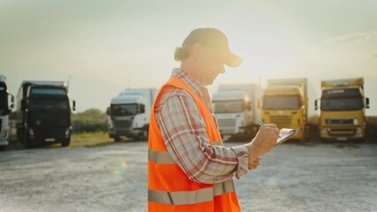 Focused Caucasian man walking on truck parking lot. Filling in information on notepad. Looking at...