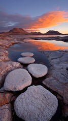 A serene landscape featuring round stones leading to a reflective water body at sunset.