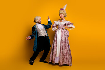 Elegant couple in vintage royal attire standing on yellow backdrop reflecting medieval and...