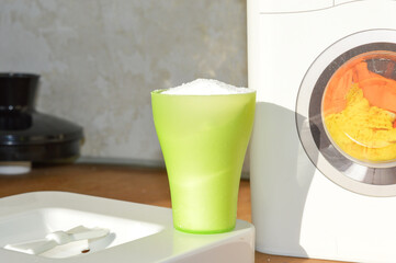 hand holding a green measuring cup filled with white laundry detergent powder washing clothes detergent drawer household cleaning products eco-friendly biodegradable non-toxic guides tutorials