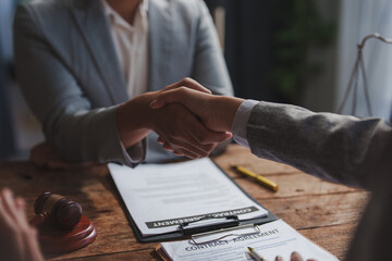 Two business professionals shaking hands over a contract agreement on a wooden desk, symbolizing...
