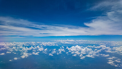 A stunning aerial view of clouds and the landscape below, captured from an airplane window. The...