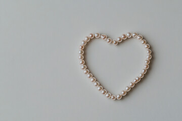 Obraz premium Pearl necklace forming heart shape on white background