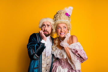 Elegant duo in medieval costumes posing against yellow backdrop with expressive gestures and...