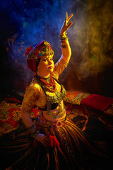 A woman in a colorful headscarf and jewelry poses in front of a wall of colorful tassels