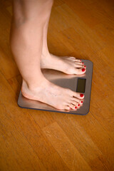 Woman feet with red nail polish on the bathroom scales 