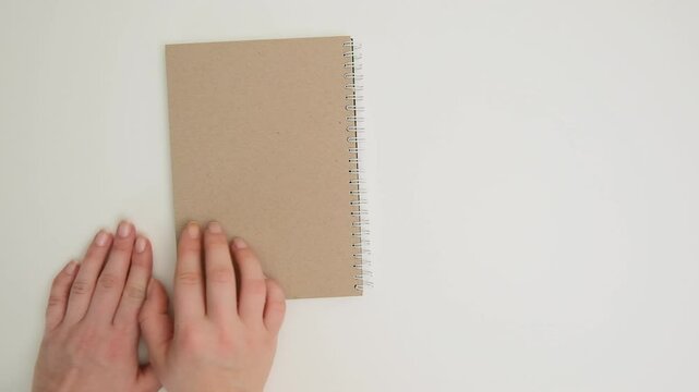 Female hands close and remove a spiral notebook from the table on a white background, top view. HD footage