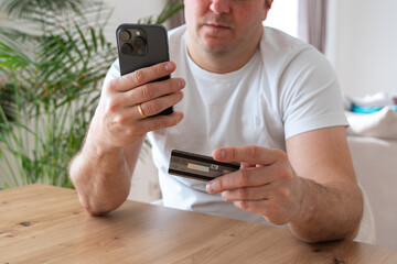 Fototapeta premium a man holding a credit card and a mobile phone sits on a chair at home in the living room. High quality photo