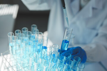Gloved scientist carefully adding blue liquid into test tube using pipette during experiment in...