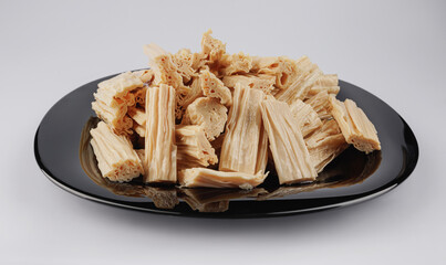 Fuzhu soy sticks in a black plate on a white background. Yuba. Top view.