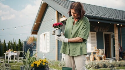 Older Caucasian woman picking up plant from pot. Carefully holding roots with wet soil not to...