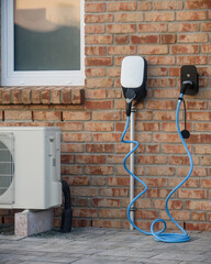 Close-up of modern brick house wall with an electric vehicle charging station with blue cable and air conditioning. Modern home with energy-efficient solutions  electric vehicle (EV) charging station.