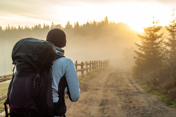 back view without face young man with big backpack in a hiking trip in the mountains background looking on summer sunrise, travel, beauty of nature