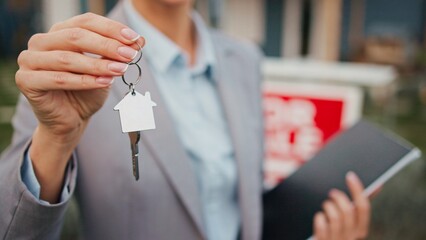Camera focus on real estate agent holding keys to house with one hand. Person in grey suit in...