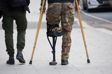 Man with prosthetic leg walking with crutches on a city street, concept of disabled people