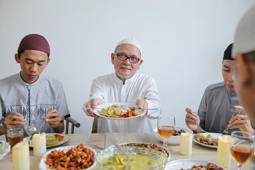Portrait Of Senior Man Showing Special Food On Plate Celebrating Eid Al Fitr At Dining Room