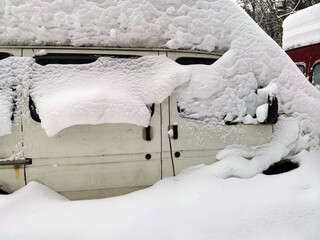 Cars covered with snow in the parking in the yard near a house