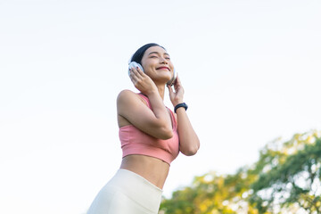 Young Asian Woman Enjoying Music with Headphones. Gen Z Female in Fitness Wear Smiling in a Natural Park Setting.