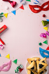 Colorful Purim celebration concept. Carnival masks, hamantaschen cookies, and festive party decorations on a pastel pink background.