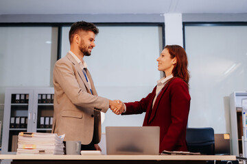 Happy businessman and businesswoman shaking hands at group board meeting.