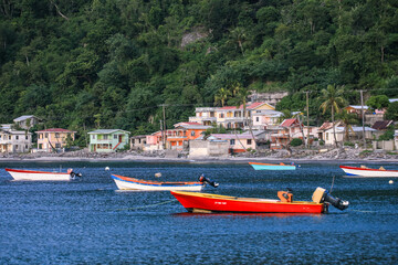 Fototapeta premium Boats bobbing gently in the blue waters off Dominica Island near colorful coastal houses
