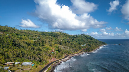 Scenic coastal road along the shore of Dominica Island with lush hills under a blue sky