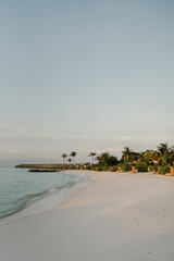 Luxury overwater villas stretch across the tranquil turquoise waters of a tropical island resort. The soft sandy beach and gentle ocean waves create a peaceful and idyllic escape at sunset in Maldives