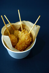 Fried chicken skewers in paper cups for take-out. Vertical fried chicken on black background for...