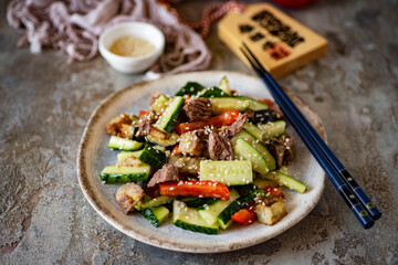 Asian cuisine: salad with beef, cucumbers and pepper for lunch. Salad with vegetables on a plate on a gray background. Close-up
