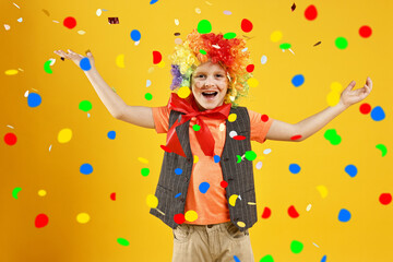 Happy boy dressed like clown under falling confetti on orange background. Party time
