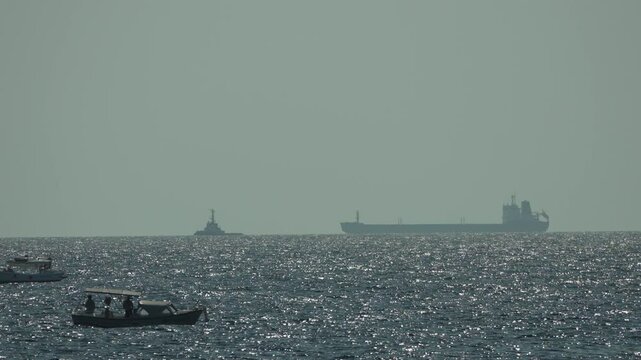 Boats, Ocean, Cargo Ship - Two small fishing boats navigate the choppy waters of the ocean as a large cargo ship sails in the distance.