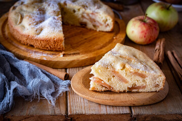 A piece of apple pie and an apple pie on a wooden table for breakfast. Sweet apple pie for dessert. Close-up