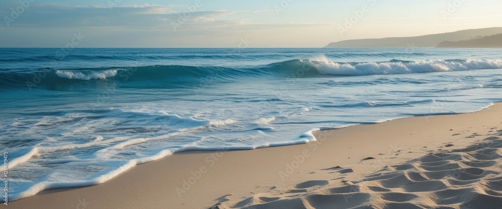 Poster sunset over calm ocean waves gently lapping on sandy beach with coastline in distance and clear blue
