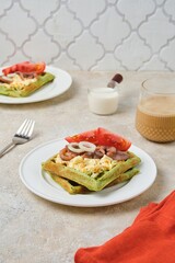 Breakfast, spinach waffles with egg salad, pickled herring and fresh tomato on a white plate on a light concrete background. Waffle recipes.