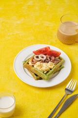 Breakfast, spinach waffles with egg salad, pickled herring and fresh tomato on a white plate on a yellow concrete background. Waffle recipes.