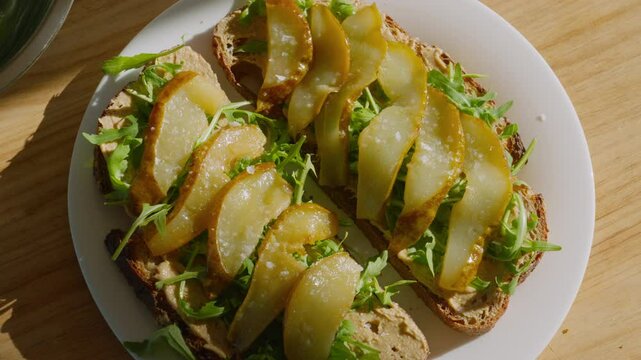 Process of preparing and serving a gourmet delicious whole wheat sourdough toast bread, topped with hummus, arugula and caramelized pears. 