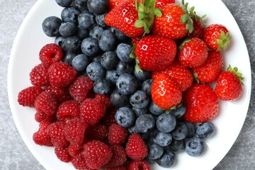 Different fresh ripe berries in bowl on light table, top view