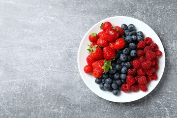Different fresh ripe berries in bowl on light table, top view