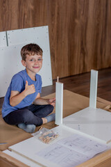 A young boy is sitting crosslegged on the floor and collect furniture enthusiastically giving a big...